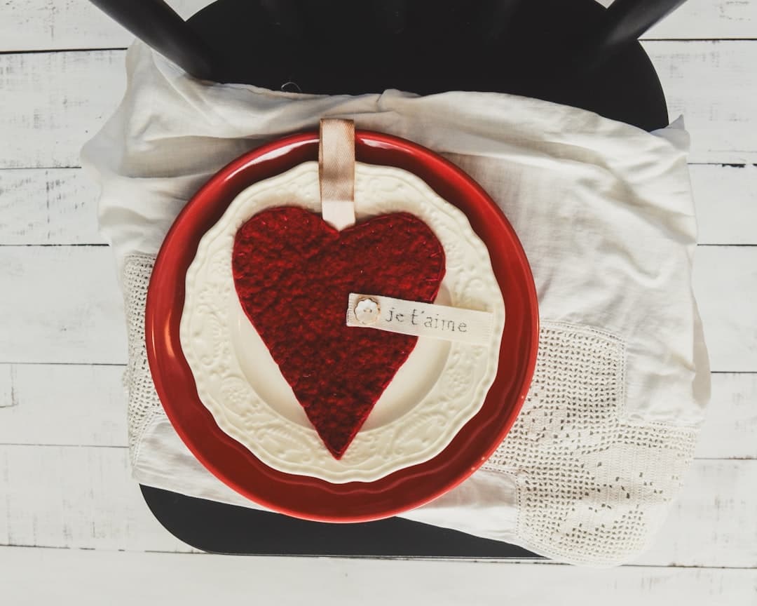 {"zh":"俯拍视角下，黑色椅子座面铺着白色棉质餐巾，其上叠放红色圆盘与雕花白瓷盘，盘中置一红色毛毡心形挂饰，挂饰系米色丝带并附有写有“Je t'aime”的小标签。","en":"From a bird's-eye view, the black chair seat is covered with white cotton napkins, upon which a red round plate and an ornate white porcelain plate are stacked. A red felt heart-shaped ornament rests in the plate, tied with a beige ribbon bearing a small tag that reads 'Je t'aime'.","ja":"俯瞰の視点では、黒い椅子の座面には白い綿製ナプキンが敷かれ、その上に赤い円盤と彫刻入りの白磁皿が重ねられています。皿の中には赤いフェルトのハート形の飾りが置かれ、ベージュのリボンで結ばれ、「Je t'aime」と書かれた小さなタグが付いています。","ko":"위에서 내려다보면 검은색 의자 좌석에는 흰색 면 소재 냅킨이 깔려 있고, 그 위에 빨간색 원형 접시와 조각 장식이 달린 백색 도자기 접시가 겹쳐져 있습니다. 접시 안에는 빨간색 펠트로 만든 하트 모양의 장식이 놓여 있으며, 베이지색 리본으로 묶인 채 'Je t'aime'라고 적힌 작은 태그가 달려 있습니다.","es":"Desde una vista cenital, el asiento de la silla negra está cubierto con servilletas de algodón blancas, sobre las que se apilan un plato redondo rojo y un plato de porcelana blanca con decoración tallada. En el plato descansa un adorno en forma de corazón de fieltro rojo, atado con una cinta de color crema que lleva una pequeña etiqueta con la inscripción 'Je t'aime'.","fr":"Vue d'en haut, l'assise de la chaise noire est recouverte de serviettes en coton blanc, sur lesquelles sont empilés un plat rond rouge et un plat en porcelaine blanche orné de sculptures. Un ornement en forme de cœur en feutre rouge repose dans le plat, attaché par un ruban beige portant une petite étiquette avec l'inscription « Je t'aime ».","de":"Aus der Vogelperspektive betrachtet ist die Sitzfläche des schwarzen Stuhls mit weißen Baumwollservietten bedeckt, auf denen ein roter runder Teller und ein weißer Porzellanteller mit Schnitzereien gestapelt sind. In dem Teller ruht ein rotes Herz-Ornament aus Filz, das mit einem beigen Band gebunden ist und ein kleines Etikett mit der Aufschrift „Je t'aime“ trägt.","it":"Dall’alto, il sedile della sedia nera è coperto da tovaglioli di cotone bianchi, su cui sono impilati un piatto rotondo rosso e un piatto di porcellana bianca decorato. Nel piatto poggia un ornamento a forma di cuore in feltro rosso, legato con un nastro beige che reca una piccola etichetta con la scritta «Je t'aime».","pt":"Vista de cima, o assento da cadeira preta está coberto com guardanapos de algodão brancos, sobre os quais são empilhados um prato redondo vermelho e um prato de porcelana branca com decoração esculpida. No prato repousa um enfeite em forma de coração feito de feltro vermelho, amarrado com uma fita bege que traz uma pequena etiqueta com a inscrição “Je t'aime”.","ru":"С высоты видно, что сиденье черного стула покрыто белыми хлопковыми салфетками, на которых сложены красный круглый тарелка и украшенная резьбой белая фарфоровая тарелка. В тарелке лежит красный фетровый орнамент в форме сердца, привязанный бежевой лентой с маленькой этикеткой, на которой написано: «Je t'aime».","vi":"Từ góc nhìn trên cao, mặt ghế của chiếc ghế màu đen được phủ bằng những chiếc khăn ăn bằng vải bông trắng, trên đó xếp chồng một đĩa tròn màu đỏ và một đĩa sứ trắng có chạm khắc. Trong đĩa đặt một món đồ trang trí hình trái tim bằng nỉ màu đỏ, được buộc bằng dây ruy-băng màu be và gắn một tấm thẻ nhỏ ghi dòng chữ \"Je t'aime\".","th":"จากมุมมองด้านบน ที่นั่งของเก้าอี้สีดำถูกปูด้วยผ้าเช็ดปากผ้าฝ้ายสีขาว บนผ้าเช็ดปากวางซ้อนกันด้วยจานทรงกลมสีแดงและจานพอร์ซเลนสีขาวแกะสลัก ภายในจานวางเครื่องประดับรูปหัวใจทำจากผ้าสักหลาดสีแดง ผูกติดกับริบบิ้นสีเบจพร้อมป้ายเล็ก ๆ ที่เขียนว่า “Je t'aime”","id":"Dari sudut pandang atas, permukaan kursi berwarna hitam dilapisi dengan serbet katun putih, di atasnya ditumpuk piring bulat berwarna merah dan piring porselen putih berukir. Di dalam piring terdapat hiasan berbentuk hati dari kain felt berwarna merah, diikat dengan pita berwarna krem yang dilengkapi label kecil bertuliskan “Je t'aime”.","hi":"ऊपर से देखने पर, काली कुर्सी का आसन सफेद कॉटन के नैपकिन से ढका हुआ है, जिसके ऊपर लाल गोल प्लेट और नक्काशीदार सफेद मिट्टी के प्लेट रखे हुए हैं। प्लेट में एक लाल फेल्ट हार्ट शेप वाला डेकोरेशन रखा है, जिसे बेज रिबन से बांधा गया है और जिस पर “Je t'aime” लिखा हुआ छोटा टैग लगा हुआ है।"}